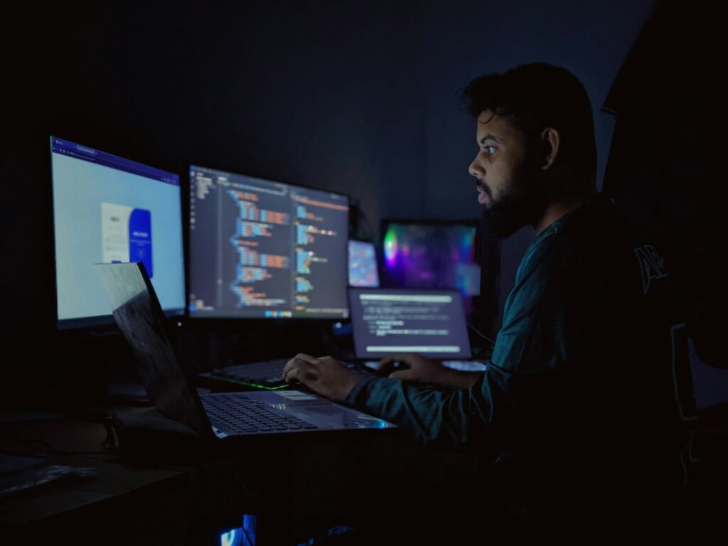 A security analyst at a multi-screen workstation reviewing logs and dashboards in a darkened room