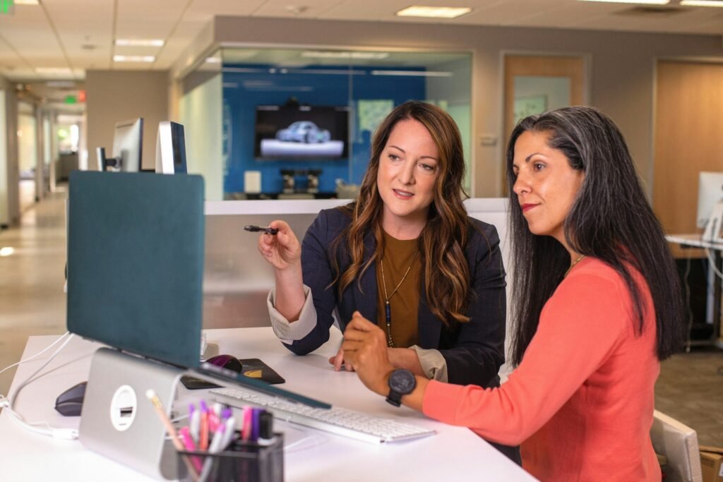 Two colleagues reviewing pipeline figures on a monitor in an open office